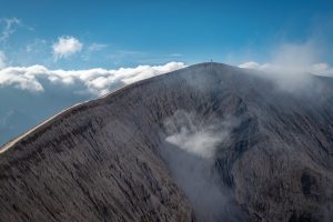 Landscape photograph of a human being on the crest of a volcanic crater.