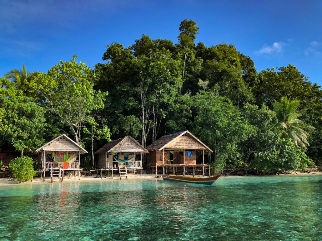 Landscape photograph of three huts on clear tropical water.