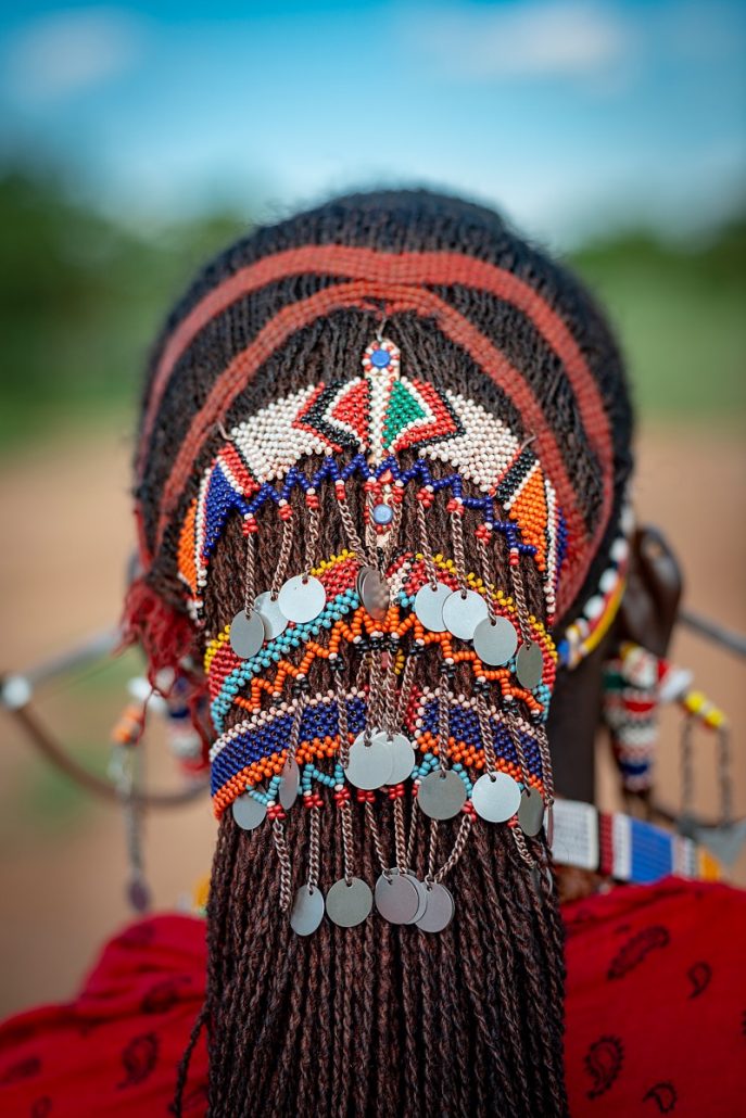 Close-up of the braided and pearl-decorated hair of a Masai warrior in traditional dress.