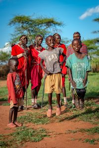 Portrait of two jumping Masai children in front of the four traditionally dressed Masai warriors in the background.