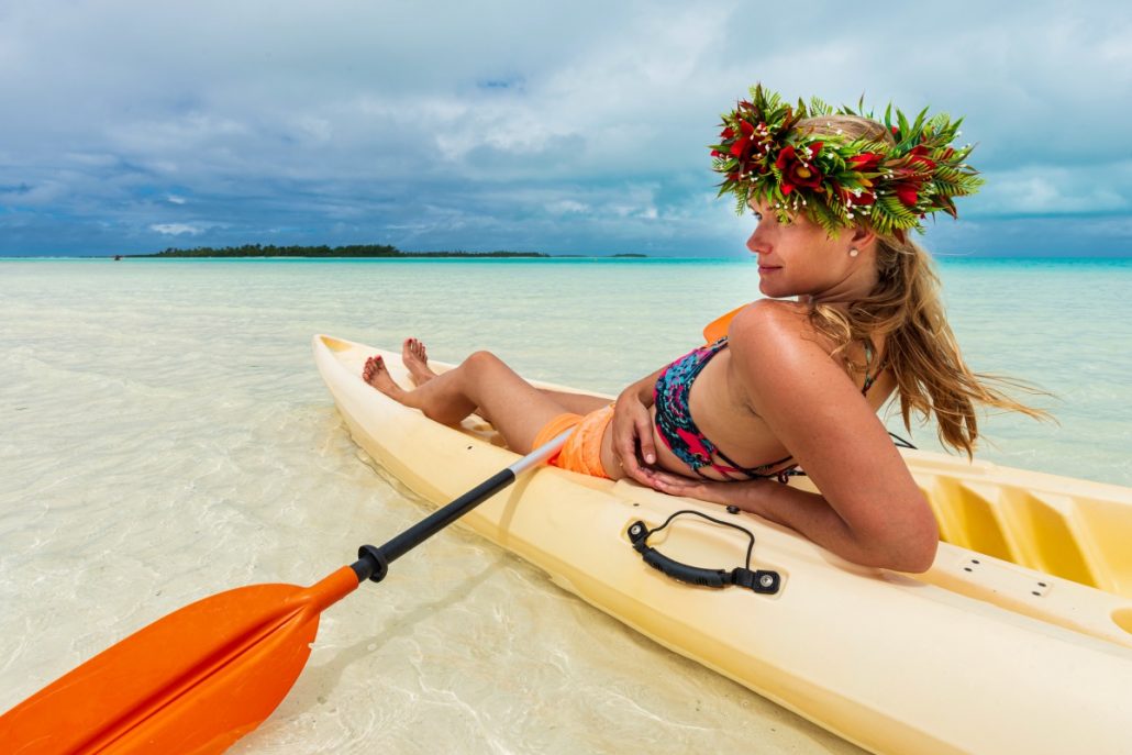Portrait of a young woman on a yellow sea kayak with a wreath of flowers on her head.