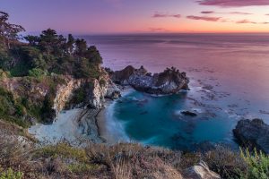 Landscape shot of a beach in a bay with waterfall at sunset.
