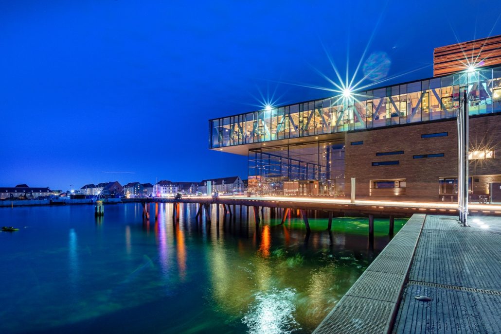 Night shot of a building on the water surrounded by a pier.