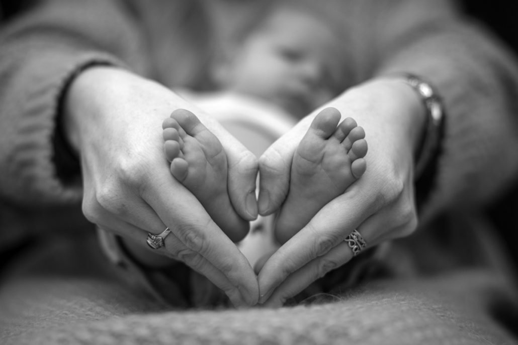 Black and white portrait of baby feet held by his mother.