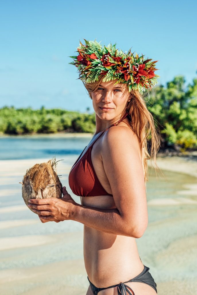 Portrait of a young woman in a red bikini with a coconut in her hand and a wreath of flowers on her head.