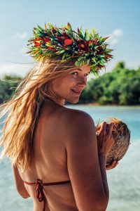 Portrait of a blonde young woman with coconut in her hand and a wreath of flowers on her head.