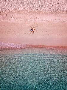 Aerial view of a couple on the beach with pink sand.