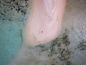 Aerial view of a woman on a sandbank with pink sand.