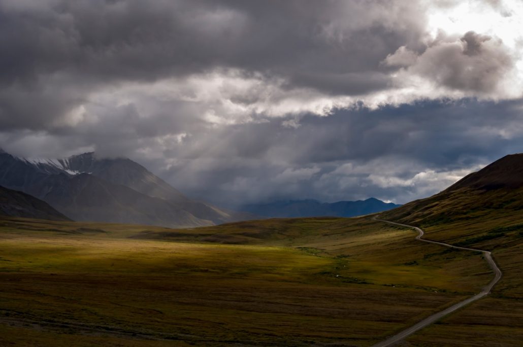 Landscape shot of a road in a cloudy valley where single rays of sunlight fall.