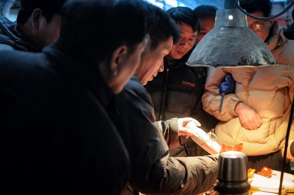 Portrait of a group of middle-aged Chinese men looking at a cricket under a lamp.