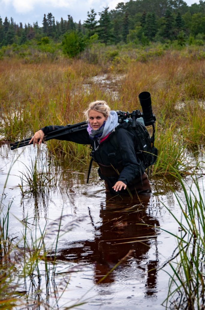 Portrait in the rain with a young female nature photographer in the swamps of Alaska with photographic equipment on her shoulders.