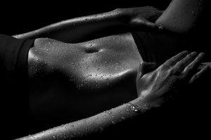 Black and white close-up and lowkey of a female belly sprinkled with water drops.